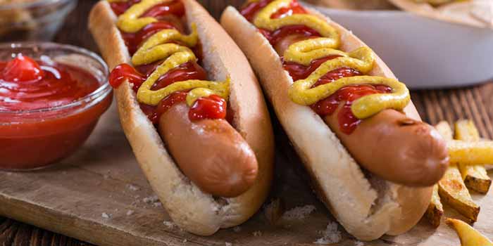 Two hot dogs with ketchup and mustard on buns, Pine Resort food and drink, fries, and ketchup.